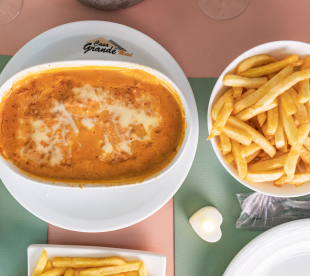 Prato com parmegiana gratinada coberta com queijo derretido acompanhada de batatas fritas em tigela branca.